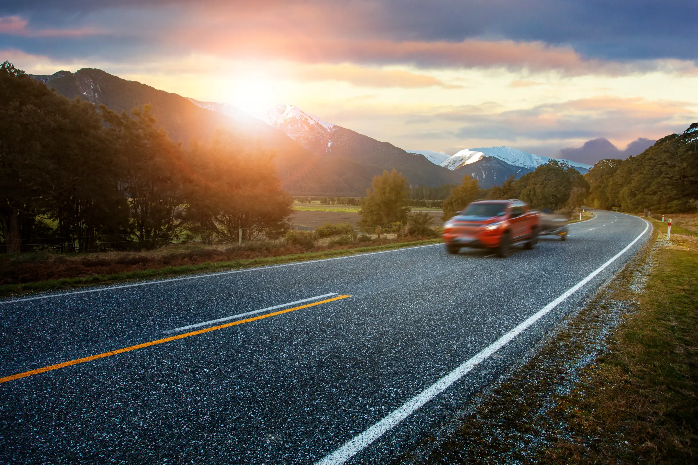 A truck rolling down an open mountain highway at sunset